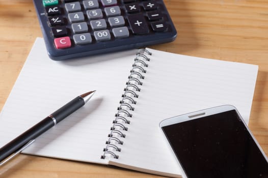 Opened notepad with blank area for text or message, pen, smart phone, and calculator on wood table