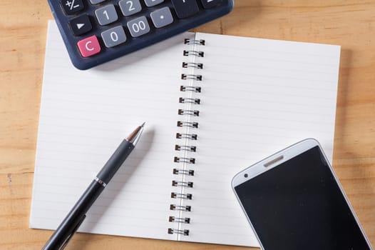 Opened notepad with blank area for text or message, pen, smart phone, and calculator on wood table