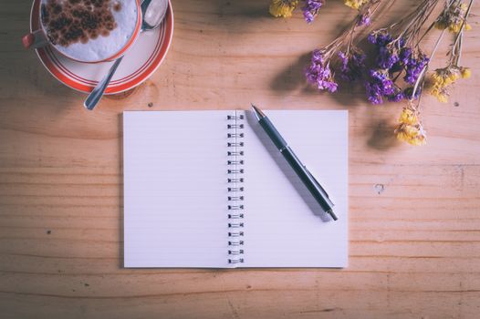 Opened notebook with blank area for text or message, pen and a cup of hot coffee on wood table in afternoon time with film filter effect