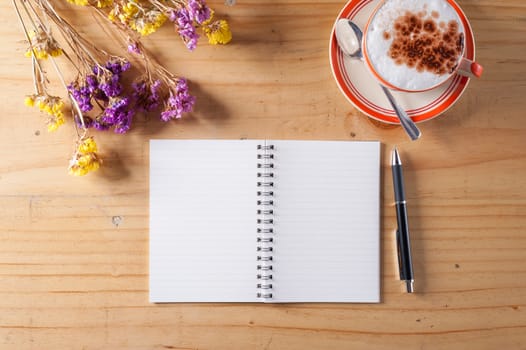 Opened notebook with blank area for text or message, pen and a cup of hot coffee on wood table in afternoon time