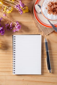 Opened notebook with blank area for text or message, pen and a cup of hot coffee on wood table in afternoon time