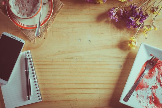 Wood table background with blank area for text or message, opened notebook, pen and a cup of hot coffee as frame in afternoon time with film filter effect