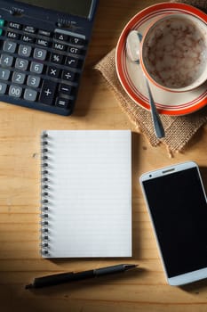 Opened notepad with blank area for text or message, pen, smart phone, and calculator on wood table in evening time with low key scene
