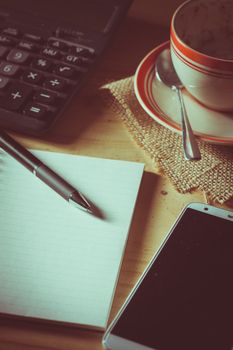 Opened notepad, pen, smart phone, and calculator on wood table in evening time with low key scene and film filter effect