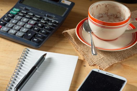 Opened notepad, pen, smart phone, and calculator on wood table in evening time with low key scene