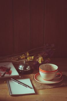 Opened notepad, pen, and a cup of hot coffee on wood table in morning time with low key scene and film filter effect