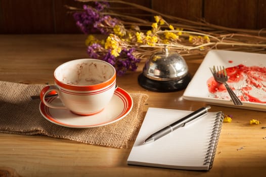 Opened notepad, pen, smart phone, and a cup of hot coffee on wood table in morning time with low key scene