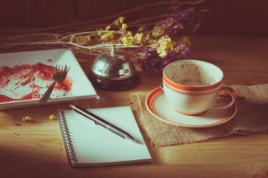 Opened notepad, pen, and a cup of hot coffee on wood table in morning time with low key scene and film filter effect