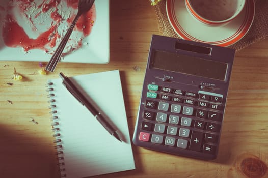 Opened notepad, pen, and calculator on wood table in evening time with low key scene and film filter effect