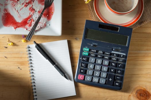 Opened notepad, pen, and calculator on wood table in evening time with low key scene