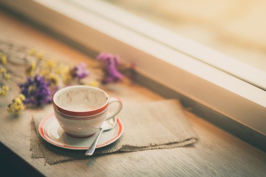 Coffee cup on wood bar beside window at coffee shop in afternoon time with film filter effect