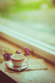 Coffee cup on wood bar beside window at coffee shop in afternoon time with film filter effect