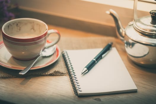 Opened notebook, pen and coffee cup on wood bar in coffee shop in afternoon time with film filter effect