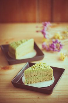 Green tea cake in black ceramic dish on wood table in afternoon time with film filter effect