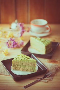 Green tea cake in black ceramic dish on wood table in afternoon time with film filter effect