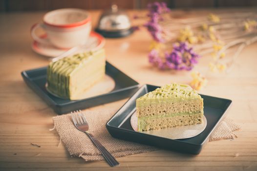 Green tea cake in black ceramic dish on wood table in afternoon time with film filter effect