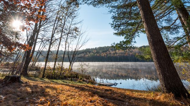 Morning sun rise revealing light fog.  Chair sits on a partially submerged dock beside a lake in Ontario, Canada.