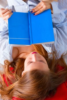 The girl in a man's shirt is reading a book in bed