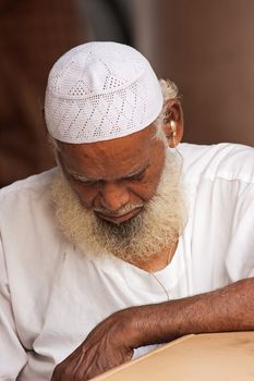 Little India, Singapore-2008. Old Hindi man with a gray beard and mustache in a traditional white robe and cap with a hearing aid sleeps at a café table and Little India district in Singapore , 2008. .Editorial.Vertical view.