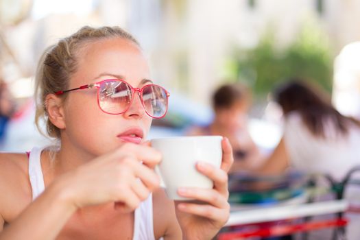 Calm casual blond lady enjoying cup of coffee outdoor in typical italian  street coffee house on warm summer day.