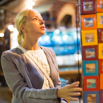 Beautiful casually dressed caucasian blond woman shopping for vacation souvenirs on crafts market in Chania, Crete, Greece.