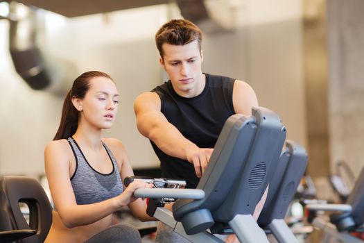 sport, fitness, lifestyle, technology and people concept - woman with trainer working out on exercise bike in gym