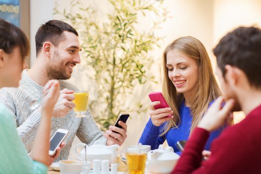 people, leisure, friendship and technology concept - group of happy friends with smartphones meeting at cafe and drinking tea