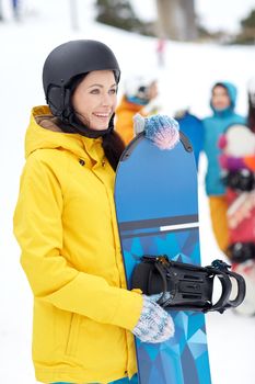 winter, leisure, extreme sport, friendship and people concept - happy young woman in helmet with snowboard and group of friends