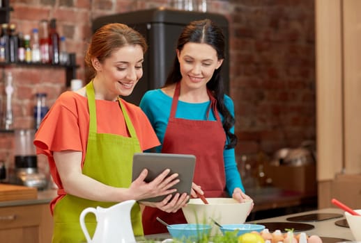 cooking class, friendship, food, technology and people concept - happy women with tablet pc computer in kitchen