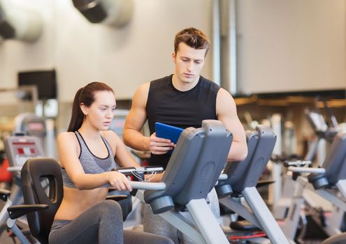 sport, fitness, lifestyle, technology and people concept - woman with trainer working out on exercise bike in gym