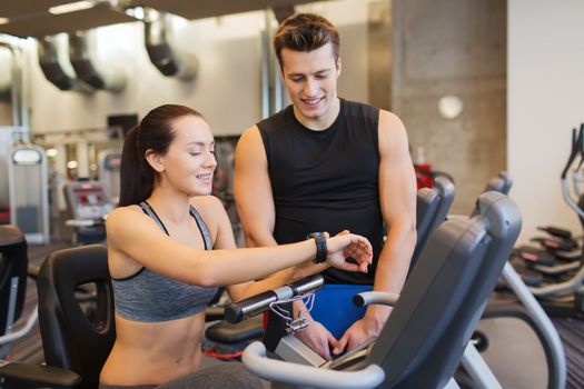 sport, fitness, lifestyle, technology and people concept - happy woman with trainer working out on exercise bike in gym