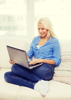 home, technology and internet concept - smiling woman sitting on the couch with laptop computer at home