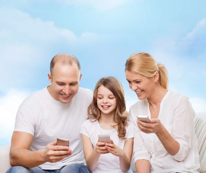 family, technology and people - smiling mother, father and little girl with smartphones over blue sky background