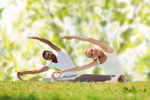 fitness, sport, yoga and people concept - happy couple stretching on mats over green tree leaves background