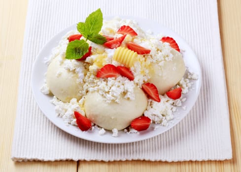 Fruit dumplings served with cottage cheese, sugar, butter and strawberries