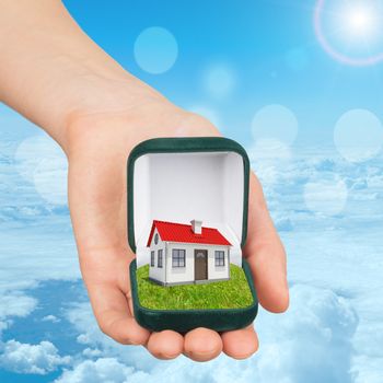 Empty ring box house in humans hand on blue sky background