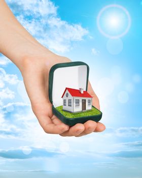 Empty ring box house in humans hand on blue sky background