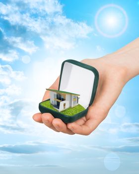 Empty ring box house in humans hand on blue sky background