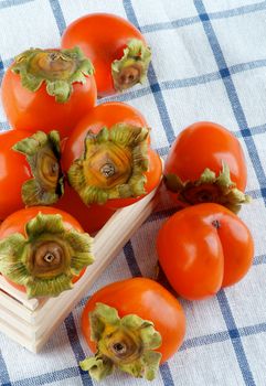 Delicious Raw Persimmon in Wooden Box closeup on Checkered Textile Napkin