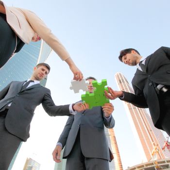 Business people assembling jigsaw puzzle near skyscrapers