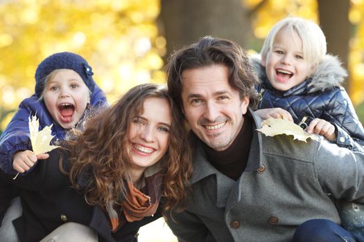 Portrait of a happy family in autumn park with maple leaves