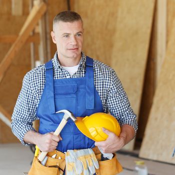 Handyman with hammer and protective helmet in house under construction