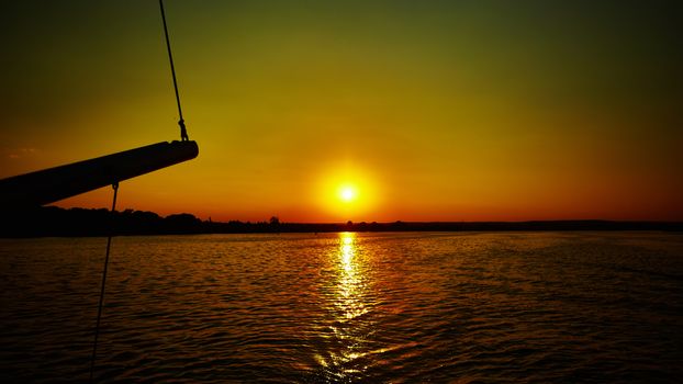 Sail boat gliding in open sea at sunset