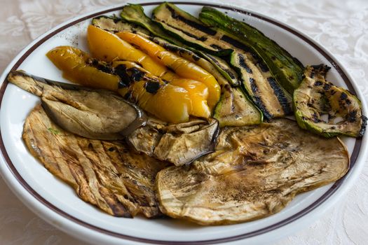 In the picture zucchini, peppers and eggplant grilled and served on white plate at restaurant.