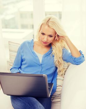 home, technology and internet concept - woman sitting on the couch with laptop computer at home