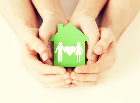 real estate and family home concept - closeup picture of male and female hands holding green paper house with family