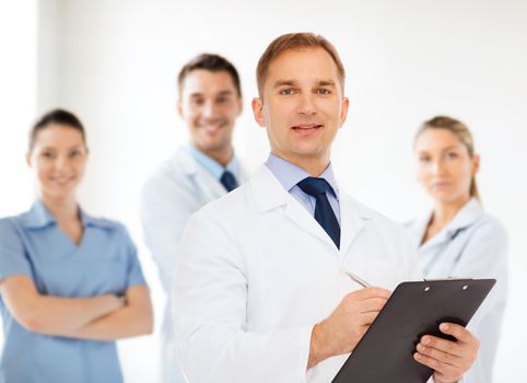 medicine, profession, teamwork and healthcare concept - smiling male doctor with clipboard writing prescription over group of medics