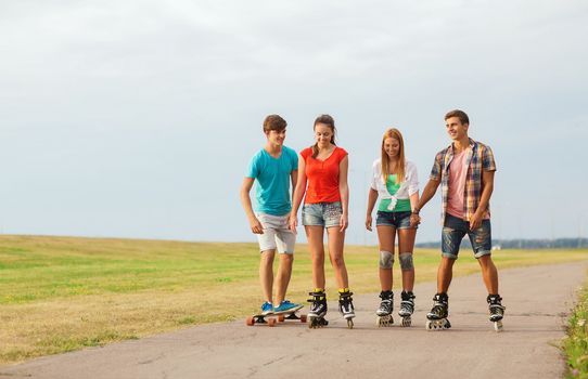 holidays, vacation, love and friendship concept - group of smiling teenagers with roller skates and skateboard riding outdoors