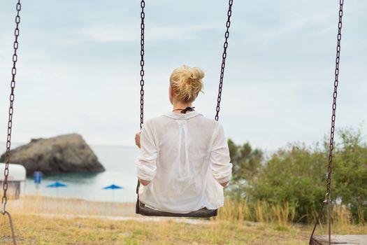 Young blonde woman sitting on the swing on beach.