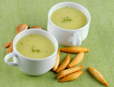 Delicious Cream Asparagus Soup in White Soup Cups with Bread Sticks and Wooden Spoons closeup on Green Napkin